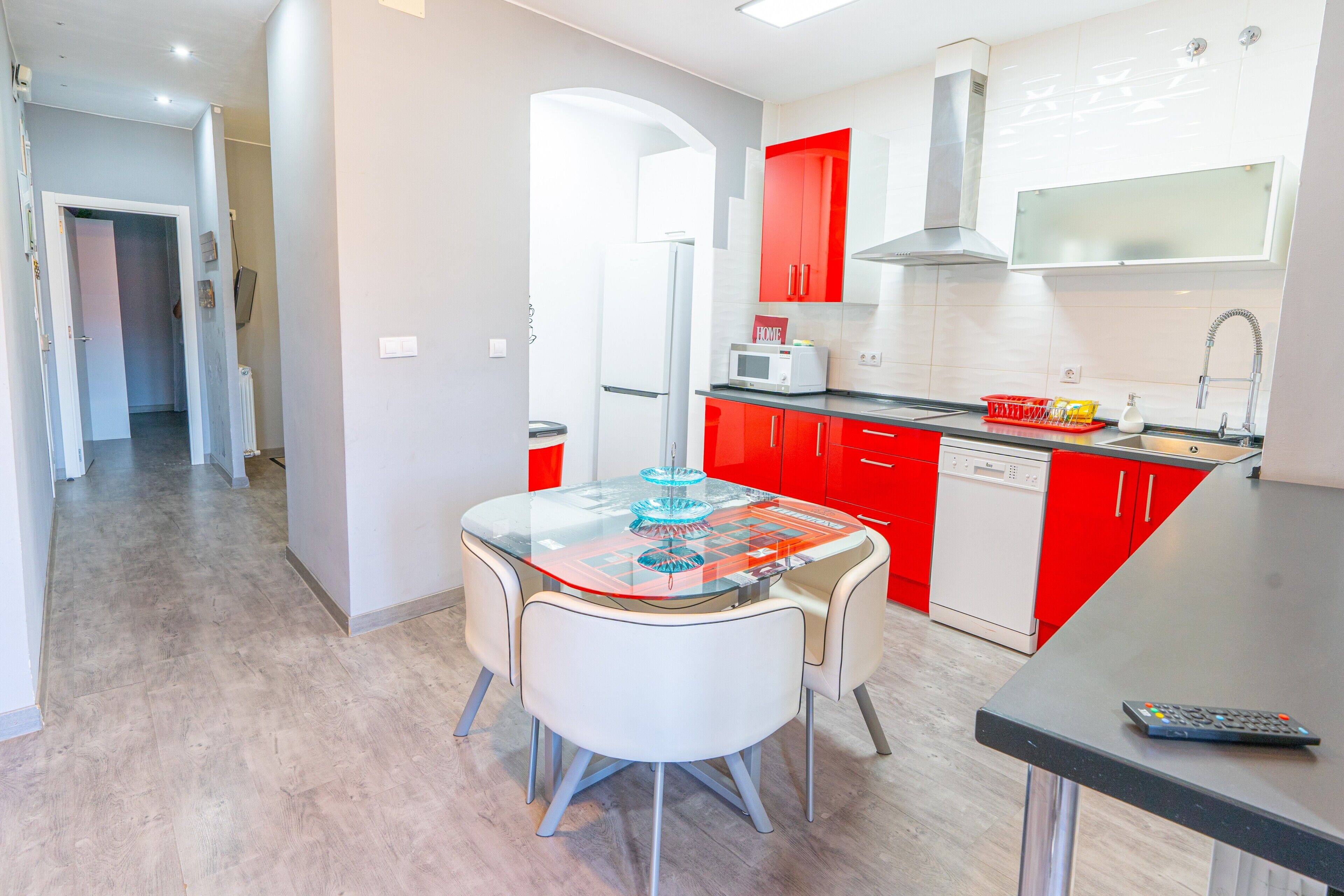 A modern kitchen with red cabinets, a glass-top dining table, and a dishwasher.
