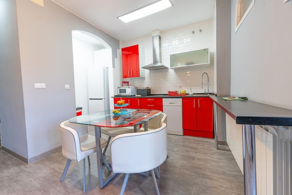 A modern kitchen with red cabinets, a glass dining table, and white chairs.