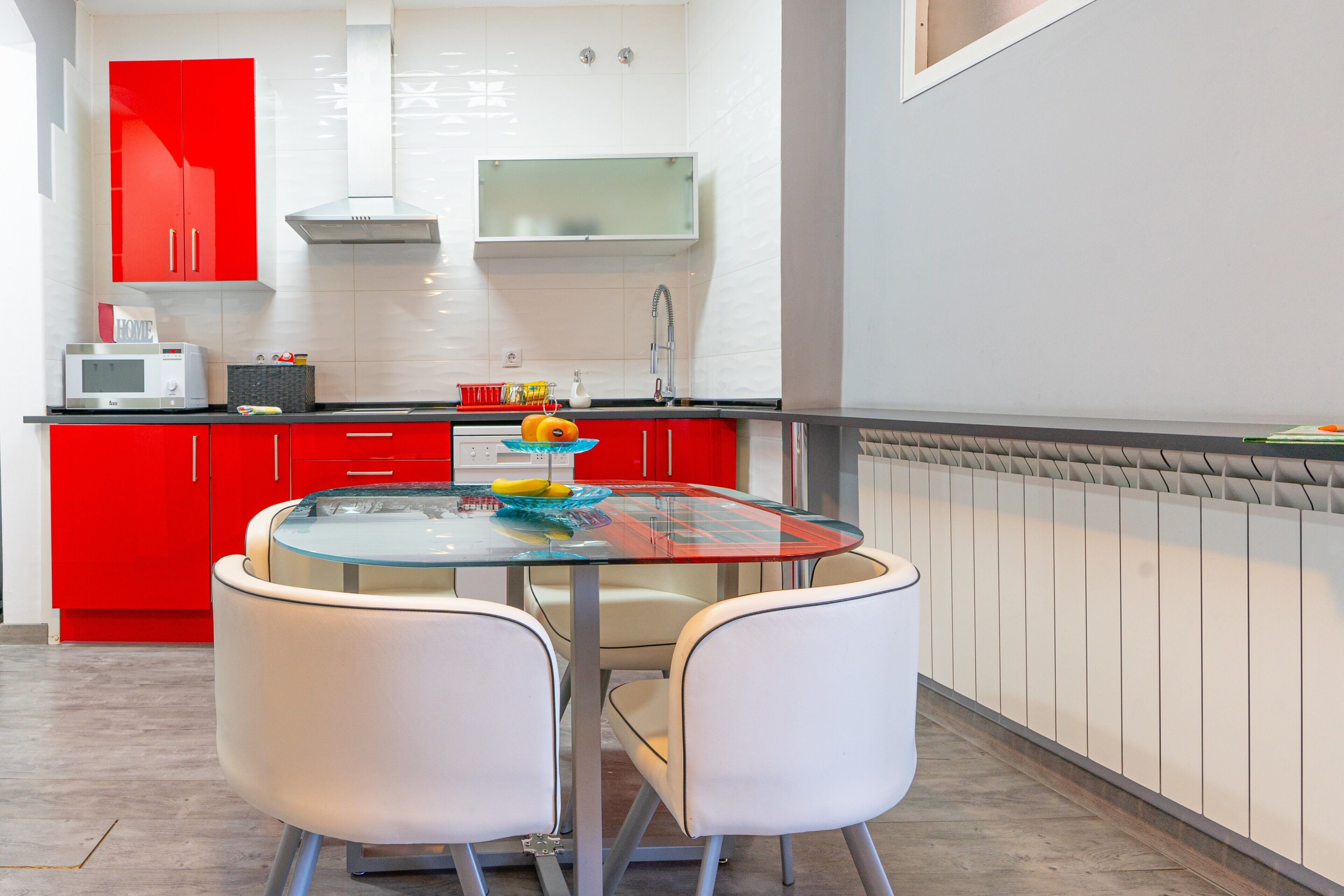 Una cocina moderna con armarios rojos, una mesa de vidrio y sillas blancas.