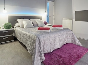 A modern bedroom with a bed, bedside tables, a nightstand, a lamp, and a radiator.
