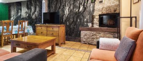A living room with a stone wall, a fireplace, a TV, wooden furniture, and a tiled floor.