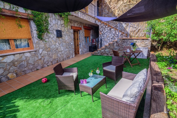 A stone building with a staircase, outdoor furniture, and a green artificial lawn.