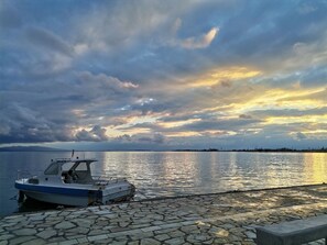 Ein Boot liegt an einem steinbelagten Ufer, das Meer ist ruhig und der Himmel bewölkt.