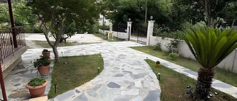 Un sendero de piedra que conduce a una puerta, rodeado de follaje y con montañas al fondo.