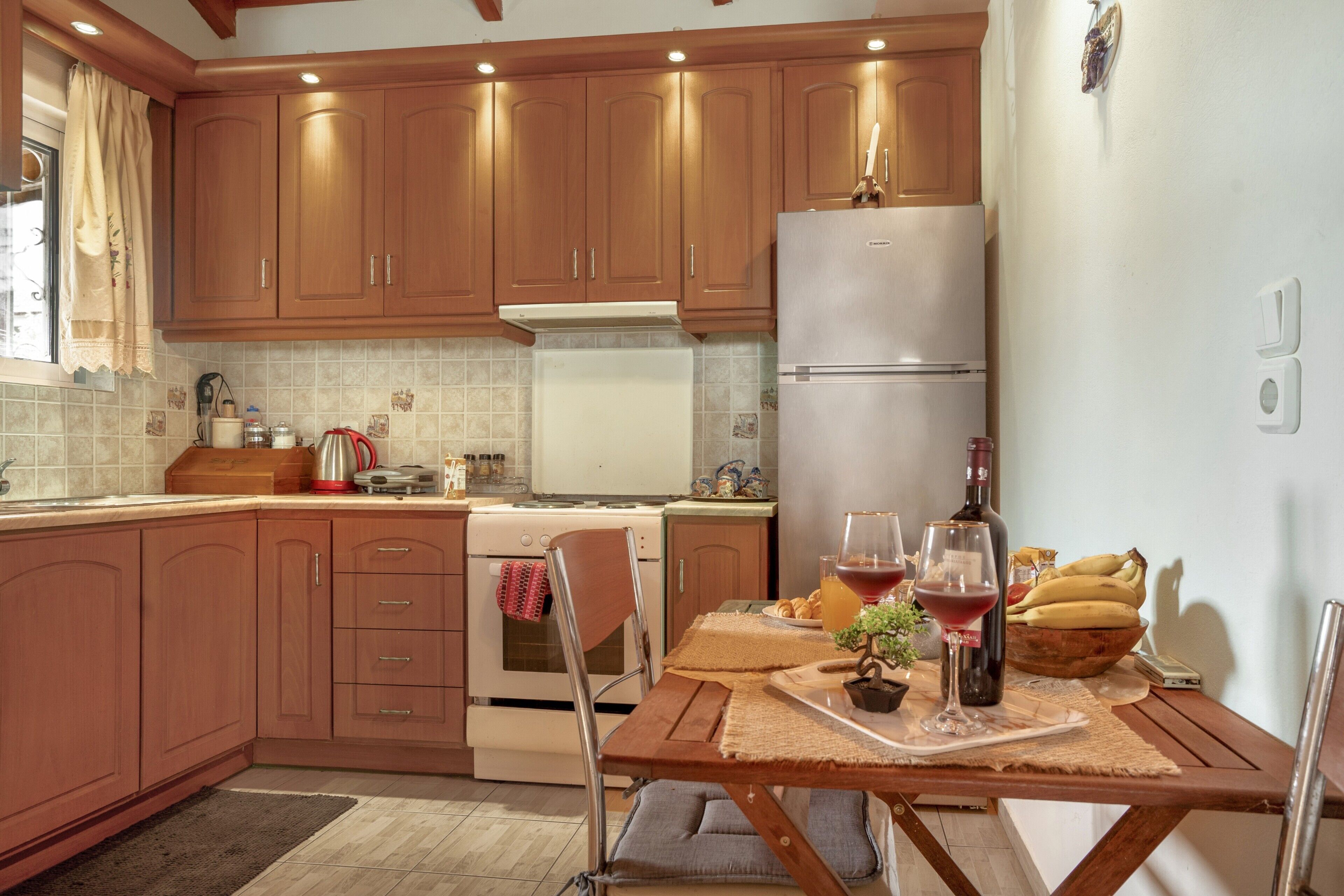 Una cocina con armarios de madera, un refrigerador, una mesa de comedor con individuales y una pequeña planta en maceta.