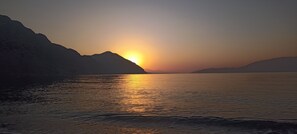 Ein Sonnenuntergang über ruhigem Gewässer, im Hintergrund Berge.