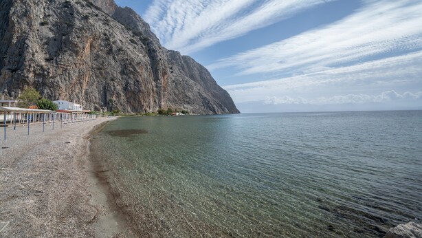 A coastal landscape with a rocky cliff, clear water, and a small building near the shore.