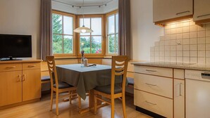 Una cocina con armarios de madera, una mesa de comedor con sillas, una ventana con cortinas y un televisor.