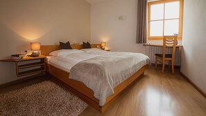 Un dormitorio con cama, mesitas de noche, escritorio, silla y ventana.