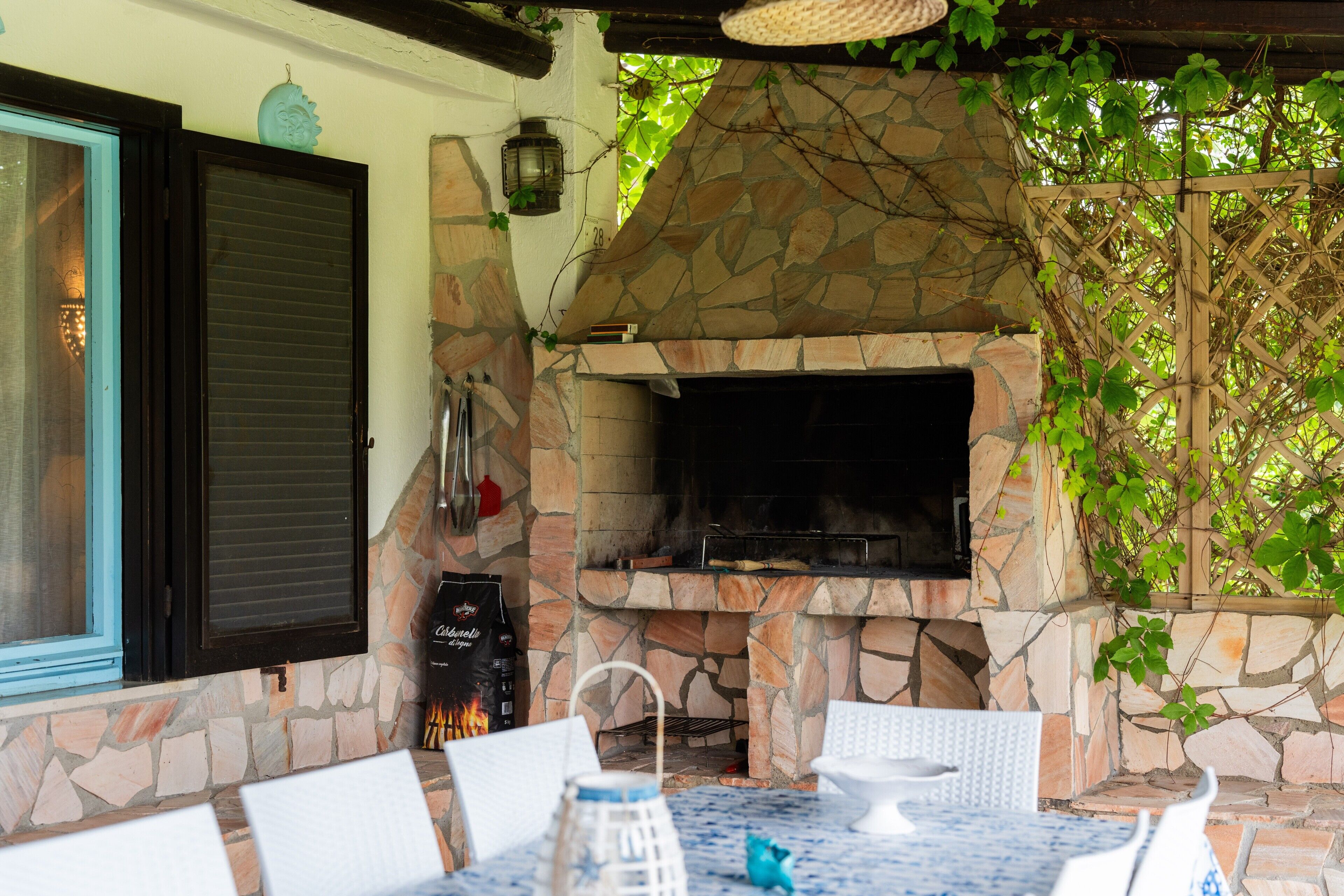 Une terrasse extérieure avec une cheminée en pierre, une table avec des chaises et une fenêtre avec des volets.