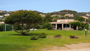 A villa with a stone facade, a large tree in the front yard, and a view of hillside houses. - Holiday Home 'Villa Tiziana' with Sea View, Wi-Fi and Air Conditioning (Costa Rei)