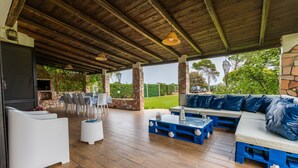 An outdoor patio with wooden flooring, stone pillars, a stone wall, a barbecue area, and a seating arrangement with blue and white furniture. - Holiday Home 'Villa Tiziana' with Sea View, Wi-Fi and Air Conditioning (Costa Rei)