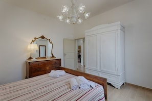 A bedroom with a bed, a dresser, a mirror, a wardrobe, and a chandelier.