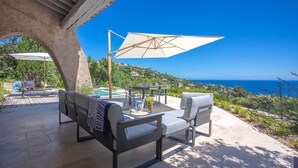 Un patio con mobiliario exterior, piscina y vista al mar.