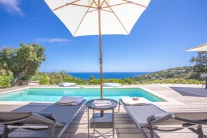 Un espace aménagé au bord de la piscine, avec des chaises longues, une table et un parasol.