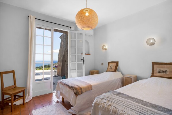 A bedroom with two beds, a view of the sea, a wicker ceiling light, and a white door. - Villa "La Louisière - Les Issambres" with Sea View, Wi-Fi, and Air Conditioning (Roquebrune-sur-Argens)