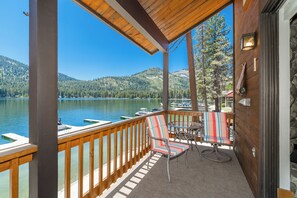 A wooden deck with a view of a lake and mountains, a striped chair, and a table.