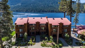 A multi-story lodge with a red roof, surrounded by greenery and a lake view.