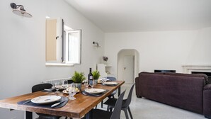 Ein Essbereich mit Holztisch, gedecktem für vier Personen, schwarzen Stühlen, einer Couch und einem kleinen Topfpflanzen.