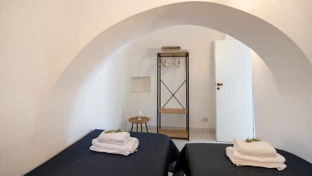 Ein Zimmer mit zwei Betten, einem kleinen Tisch, einem Regal und einer Rundbogenöffnung.