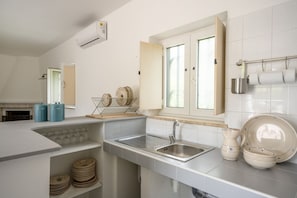 A modern kitchen with a built-in sink, a window with open shutters, and a stainless steel range hood.