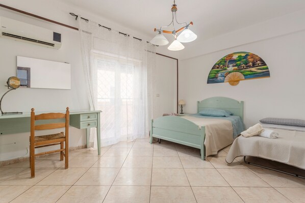 A bedroom with a bed, a desk, a chair, a window with curtains, a wall-mounted air conditioner, and a wall art piece.