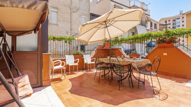Eine Terrasse im Freien mit Tisch, Stühlen, einem großen Sonnenschirm und Kübelpflanzen.