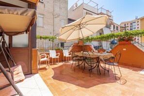An outdoor patio with a table and chairs, a large umbrella, and potted plants.