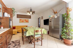 Un comedor con una mesa preparada para cuatro personas, un sofá, un refrigerador y una televisión.