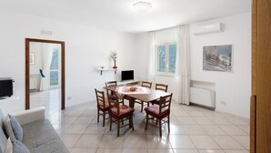 A dining area with a round table, six chairs, a TV, and a window with curtains. - Apartment 'Appartamento Capri' with Sea View, Wi-Fi and Air Conditioning (Massa Lubrense)