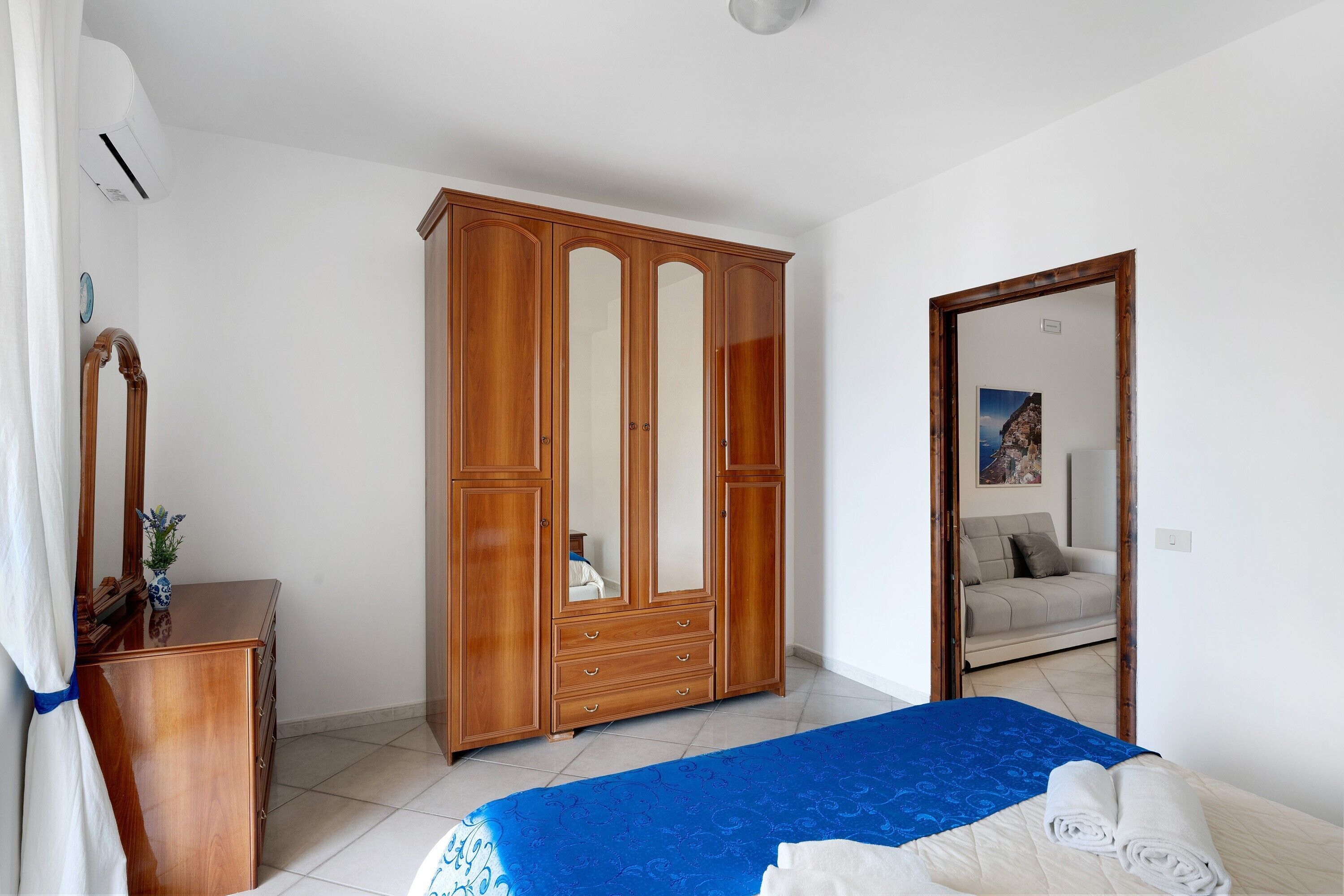 A bedroom with a bed, a wooden wardrobe, a dresser, and a mirror.