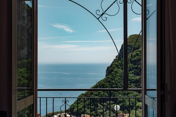 A balcony with a view of a coastal landscape, including a body of water and a hill with vegetation.