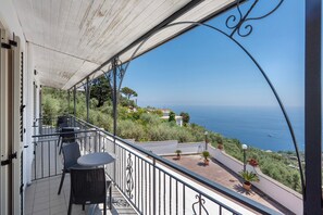 Un balcone con mobili da esterno, vista sul mare e un pendio con edifici.