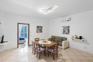 Un comedor con una mesa, sillas y un sofá. Se observa una ventana con vista a un edificio.
