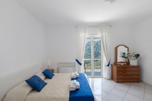 Quarto com cama, cómoda, espelho e vista para o verde através de uma janela.