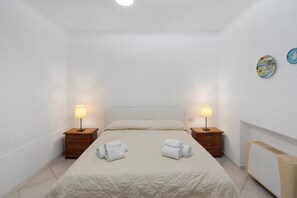 Camera d'albergo con un letto, due comodini con lampade, un termosifone e due opere d'arte appese al muro.