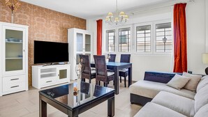 Un salon comprenant un téléviseur, une table à manger, des chaises, un canapé et une table basse en verre.