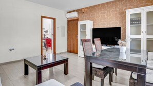 Un salon moderne avec une table à manger en verre, des chaises en osier, un téléviseur à écran plat et un meuble blanc.