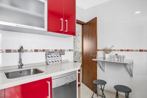 Une cuisine avec des placards rouges, un lave-vaisselle, un évier et une porte en bois.