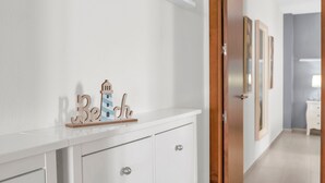 Une commode blanche avec des tiroirs, une petite étagère ornée d’objets décoratifs et une enseigne en bois portant le mot « Reich », fixée au mur.