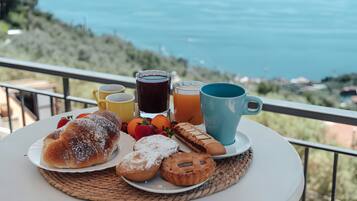 A table with breakfast items including pastries, fruits, and drinks, set against a scenic backdrop.