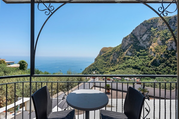 Un balcon avec une table et des chaises, donnant sur un paysage cĂŽtier avec une montagne et la mer.