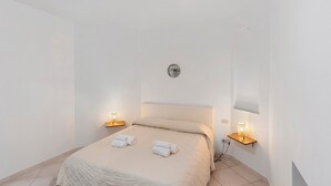 Un dormitorio minimalista con cama, dos lámparas de noche y un aplique de pared.