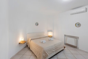 Un dormitorio con cama, lámparas de noche, un radiador y dos relojes de pared.