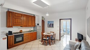 A kitchen with wooden cabinets, a dining table with chairs, a sofa, and a TV. - Apartment 'Appartamento Napoli' with Sea View, Wi-Fi and Air Conditioning (Massa Lubrense)