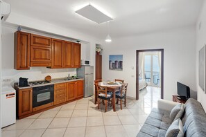 Une cuisine avec des meubles en bois, une table à manger avec des chaises, un canapé et un téléviseur.