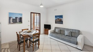 A dining area with a table and chairs, a sofa, a television, and two wall-mounted pictures. - Apartment 'Appartamento Napoli' with Sea View, Wi-Fi and Air Conditioning (Massa Lubrense)