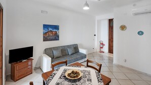 A living room with a sofa, TV, dining table, and a painting on the wall. - Apartment 'Appartamento Napoli' with Sea View, Wi-Fi and Air Conditioning (Massa Lubrense)