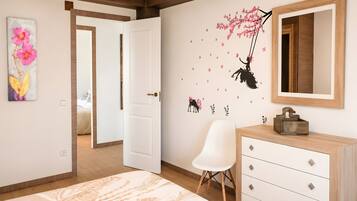 A bedroom with a bed, a dresser, a chair, a door, and a wall with a floral painting and a wall decal.