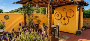 Une terrasse avec une table et des chaises en bois, des plantes en pot et des éléments décoratifs muraux.